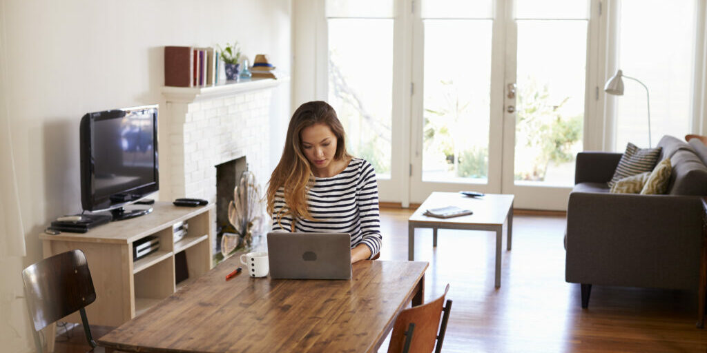 Woman Working From Home Using Laptop On Dining Table